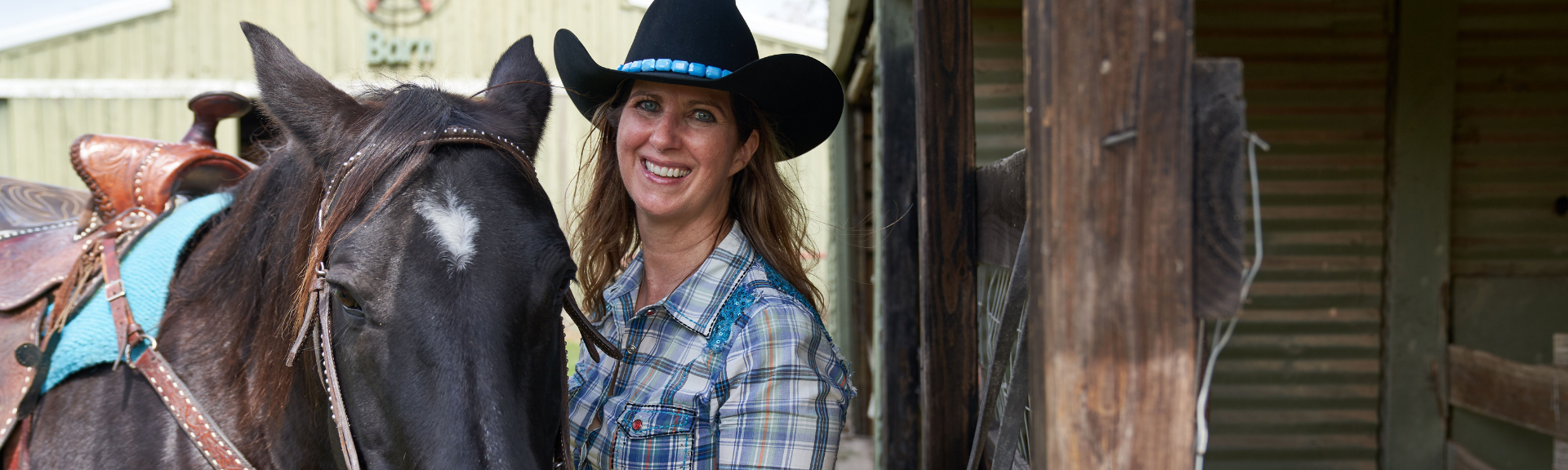 woman in cowboy hat standing next to horse and smiling